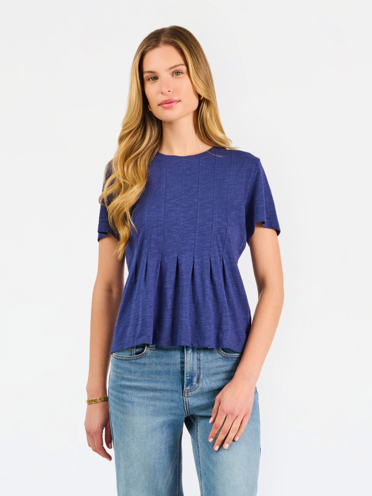 A woman modeling a short-sleeve peplum top in a heathered periwinkle blue color, paired with light-wash blue jeans, against a plain white studio background.