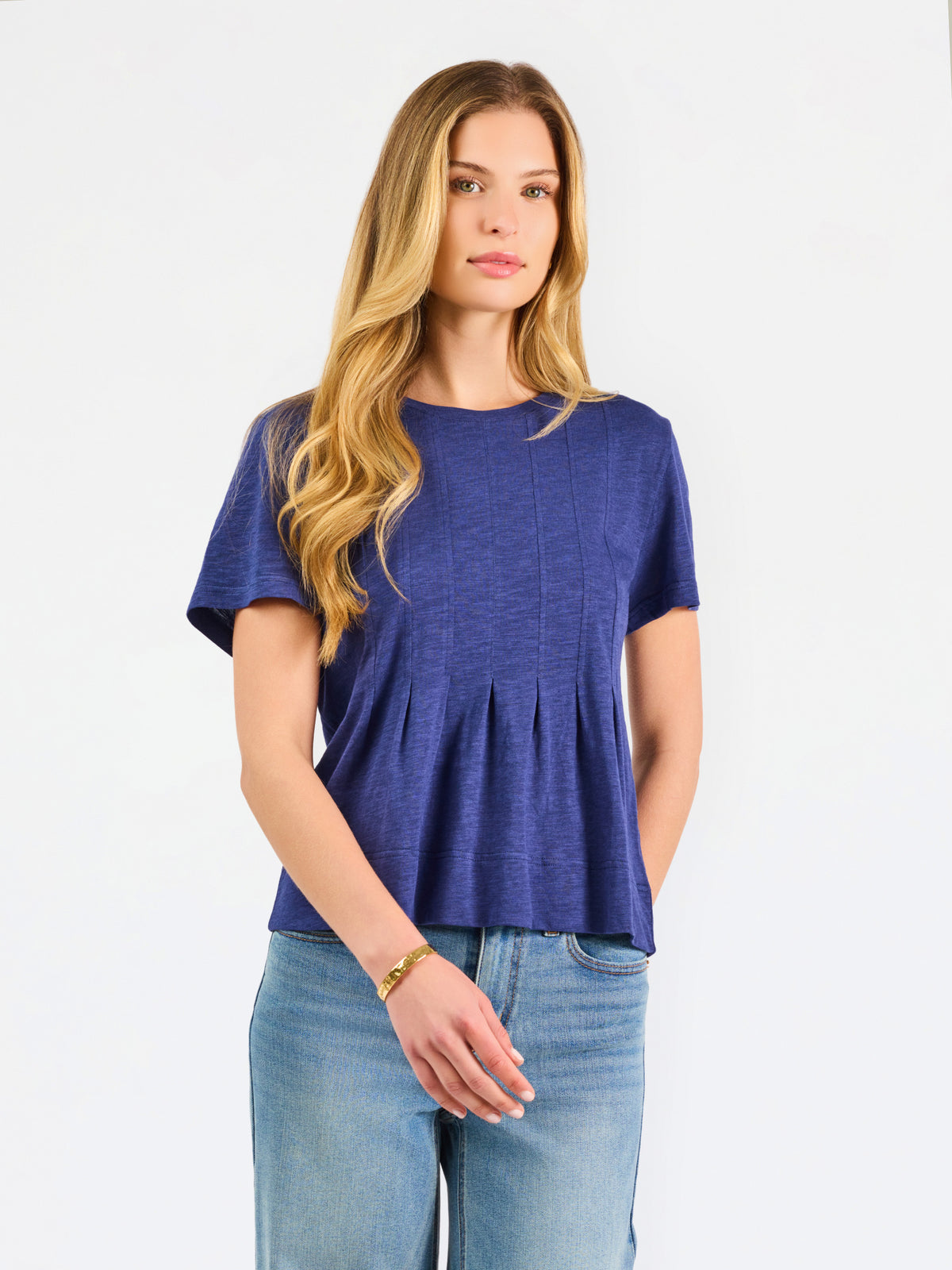 A woman modeling a short-sleeve peplum top in a heathered periwinkle blue color, paired with light-wash blue jeans, against a plain white studio background.