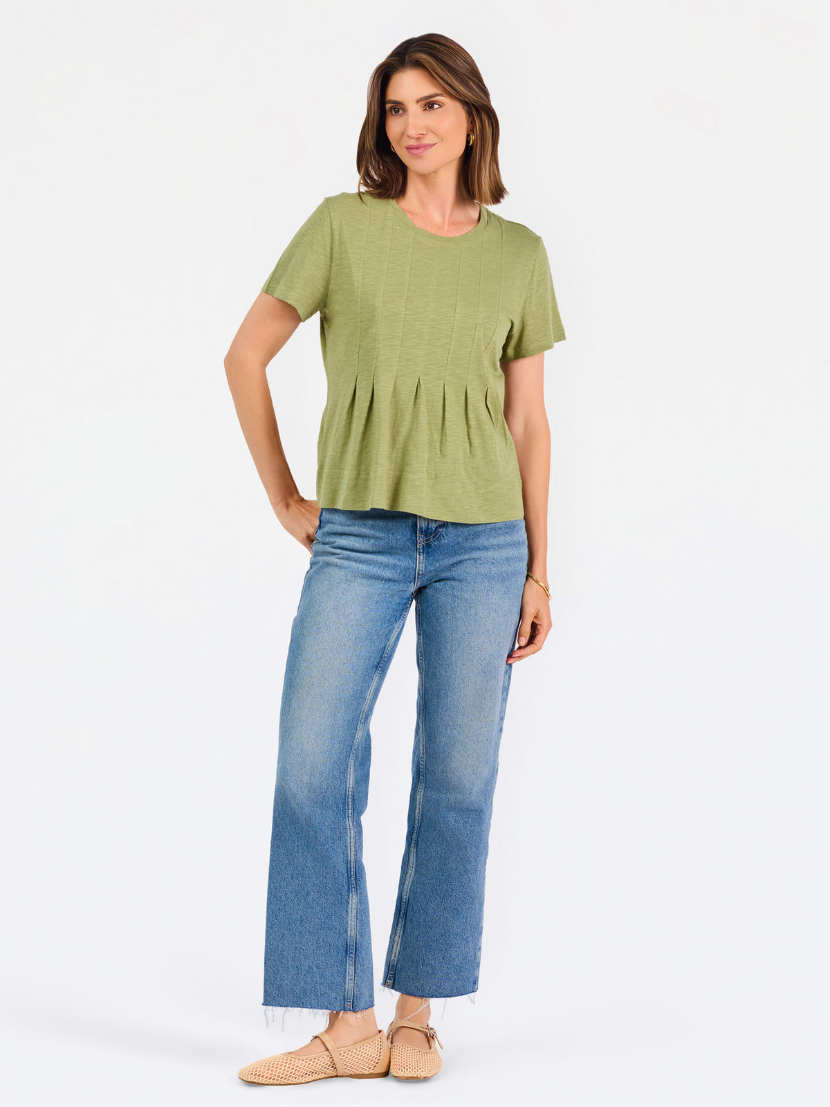 A woman wearing a sage green short-sleeve top with a gathered peplum hem, paired with blue jeans, against a plain white background.