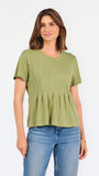 A woman wearing a sage green short-sleeve top with a gathered peplum hem, paired with blue jeans, against a plain white background.
