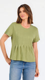 A woman wearing a sage green short-sleeve top with a gathered peplum hem, paired with blue jeans, against a plain white background.