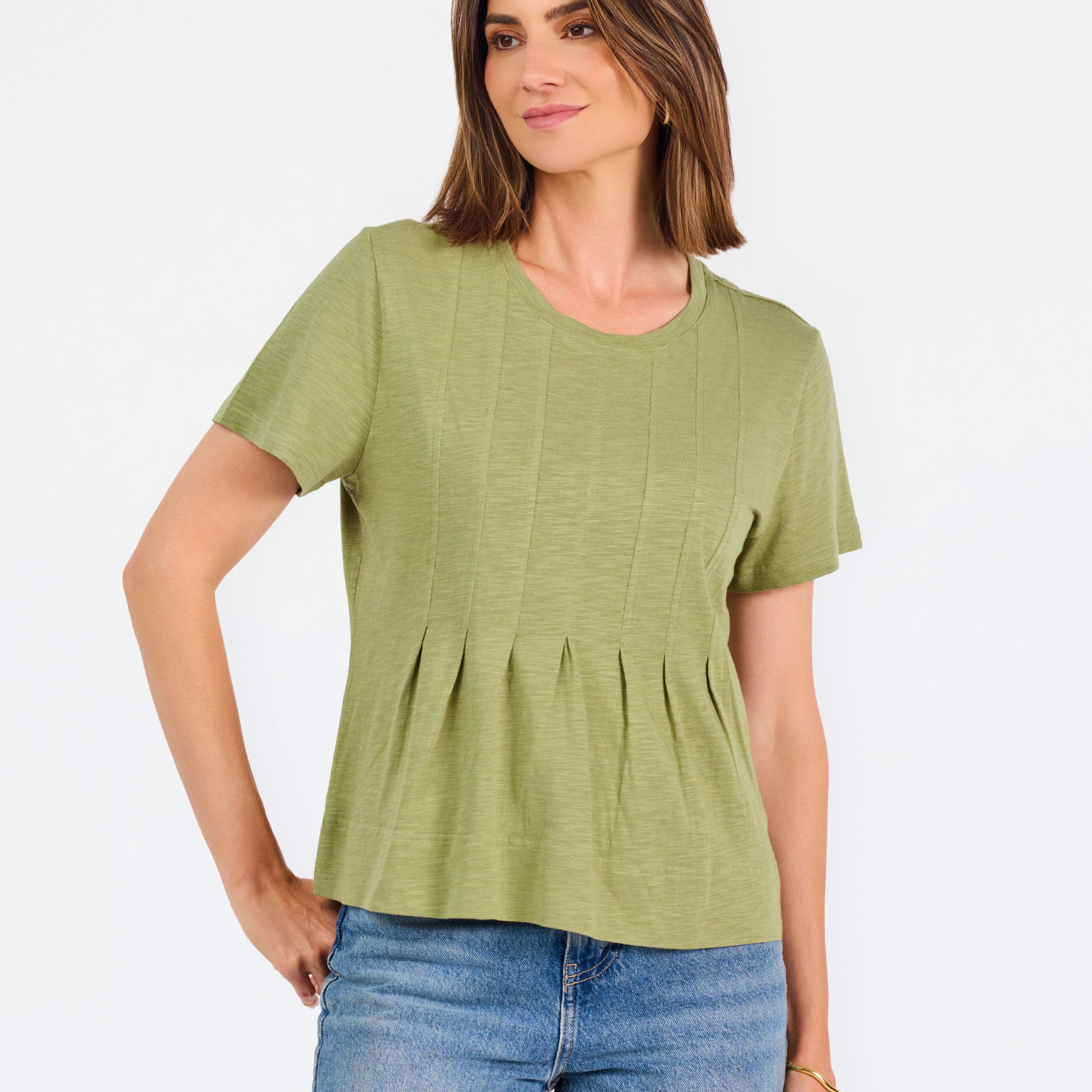 A woman wearing a sage green short-sleeve top with a gathered peplum hem, paired with blue jeans, against a plain white background.