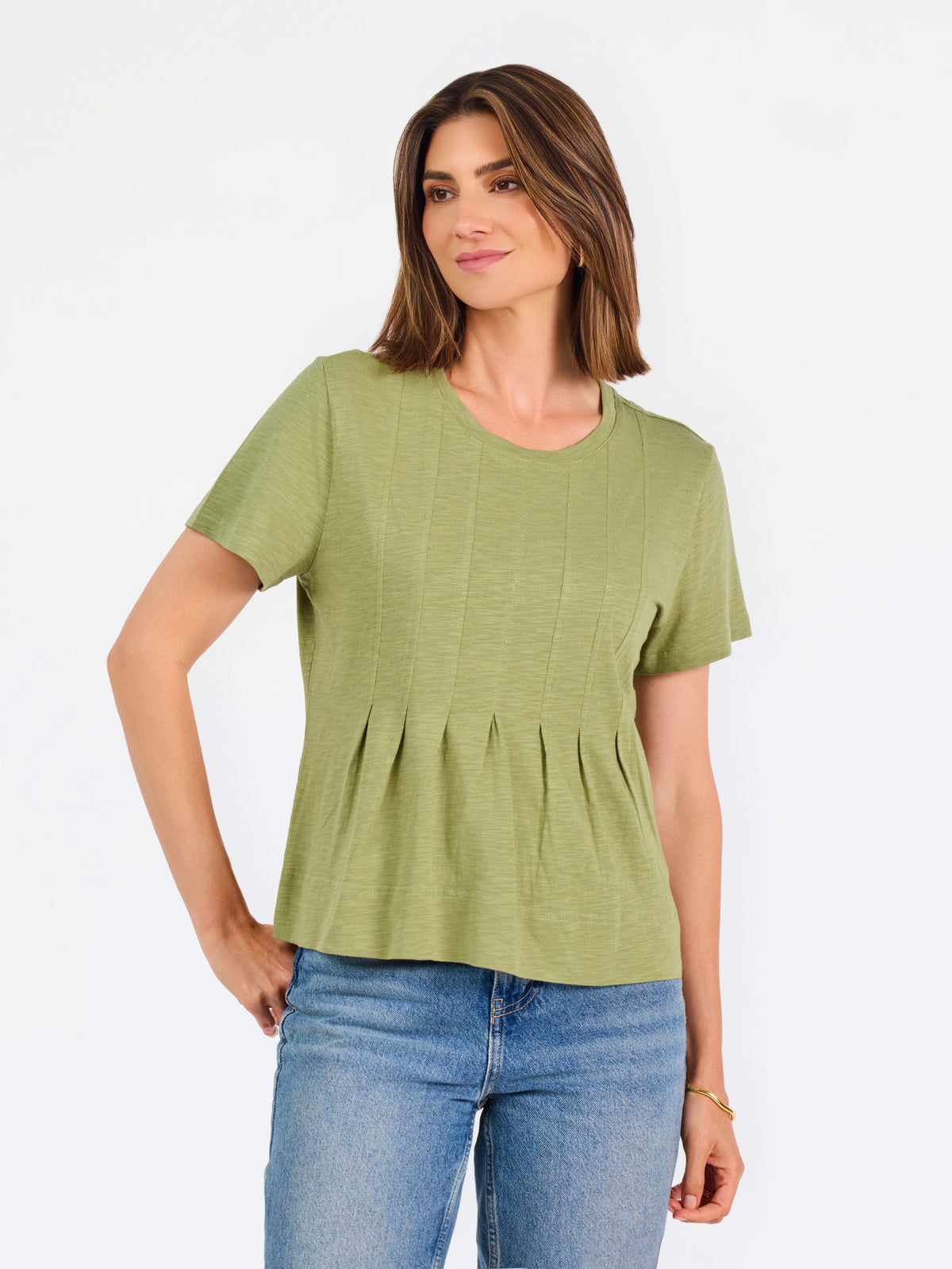 A woman wearing a sage green short-sleeve top with a gathered peplum hem, paired with blue jeans, against a plain white background.
