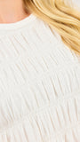 Close-up of a cream-colored smocked cotton top with horizontal gathered seams, worn by a model with blonde hair.