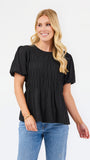 A woman modeling a black short-sleeve peplum top with puff sleeves and a smocked bodice, paired with blue jeans, against a plain white studio background.
