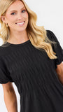 A smiling blonde woman wearing a black short-sleeve dress with a smocked bodice and puffed sleeves, photographed against a clean white studio background.