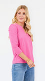 A woman modeling a bright pink three-quarter sleeve top with a split neckline, paired with blue jeans, against a plain white studio background.