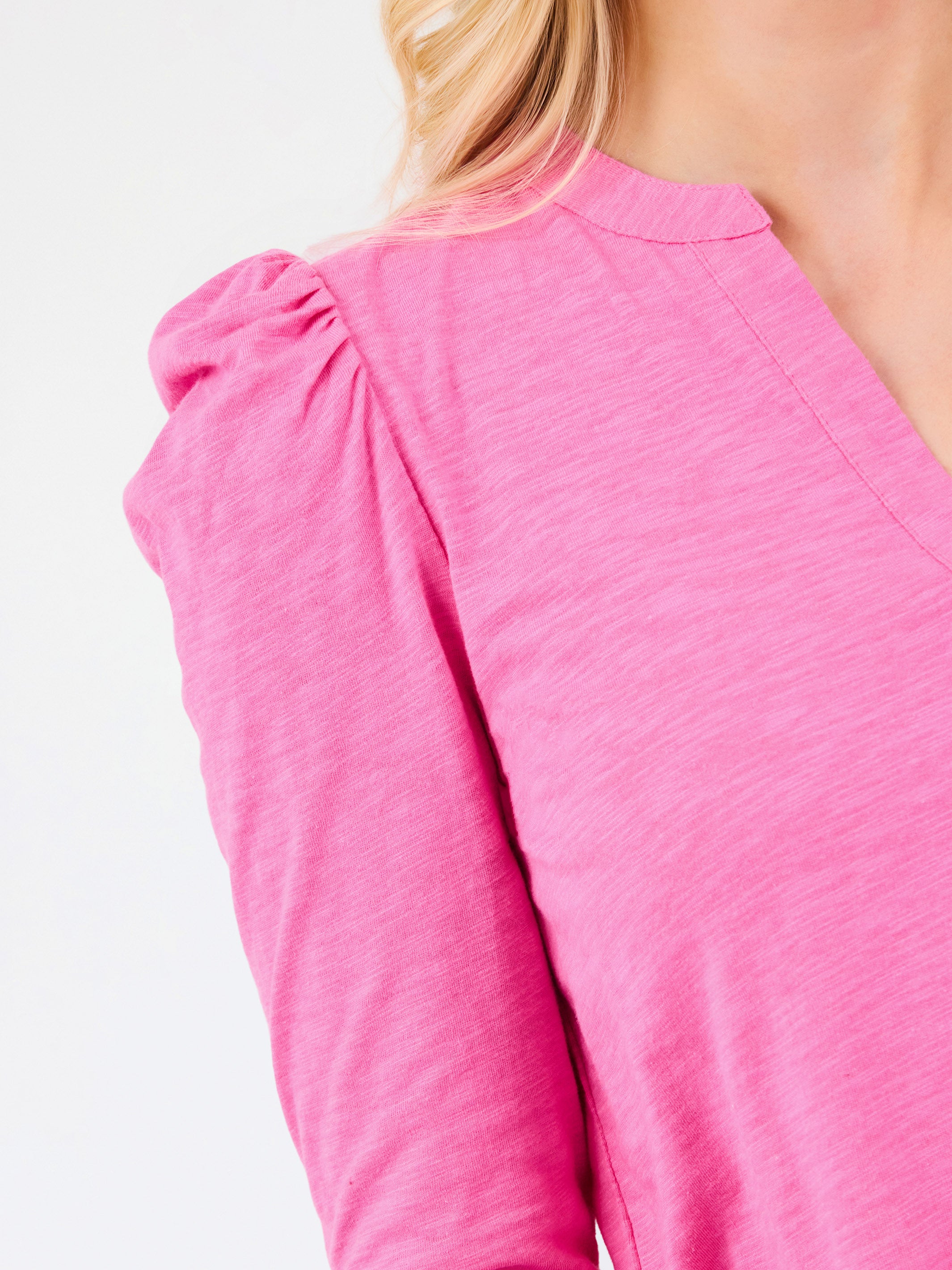 A close-up of a woman wearing a bright pink long-sleeve top with a gathered puff sleeve and a rounded neckline, shown against a plain white background.