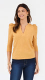 A woman modeling a mustard yellow three-quarter sleeve top with puffed shoulders and a split V-neckline, paired with dark blue jeans against a plain white background.