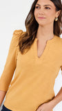 A woman wearing a mustard yellow three-quarter sleeve top with puff sleeves and a split V-neckline, shown against a plain white background.