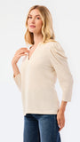 A blonde woman modeling a white long-sleeve knit top with a V-neck and puffed shoulders, paired with blue jeans, against a plain white studio background.