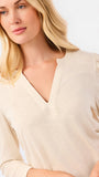 A blonde woman modeling a white long-sleeve knit top with a V-neck and puffed shoulders, paired with blue jeans, against a plain white studio background.