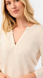 A blonde woman modeling a white long-sleeve knit top with a V-neck and puffed shoulders, paired with blue jeans, against a plain white studio background.