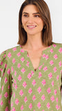 A woman modeling a green long-sleeve blouse with a pink floral pattern, puff sleeves, and a split V-neckline, paired with blue jeans against a plain white background.