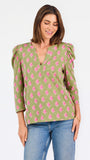A woman modeling a green long-sleeve blouse with a pink floral pattern, puff sleeves, and a split V-neckline, paired with blue jeans against a plain white background.