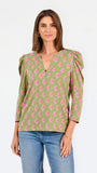 A woman modeling a green long-sleeve blouse with a pink floral pattern, puff sleeves, and a split V-neckline, paired with blue jeans against a plain white background.