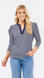 A woman modeling a navy and white horizontally striped long-sleeve top with a split V-neckline, paired with light blue jeans, against a plain white studio background.