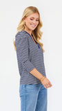 A woman modeling a navy and white horizontally striped three-quarter sleeve top with a V-neck, paired with blue jeans, against a plain white studio background.
