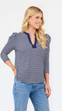 A blonde woman modeling a navy and white horizontally striped long-sleeve top with a split V-neckline, paired with blue jeans, against a plain white studio background.