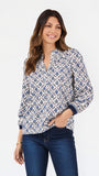 A woman modeling a long-sleeve button-up blouse with a blue and white geometric pattern, paired with dark blue jeans, against a plain white studio background.
