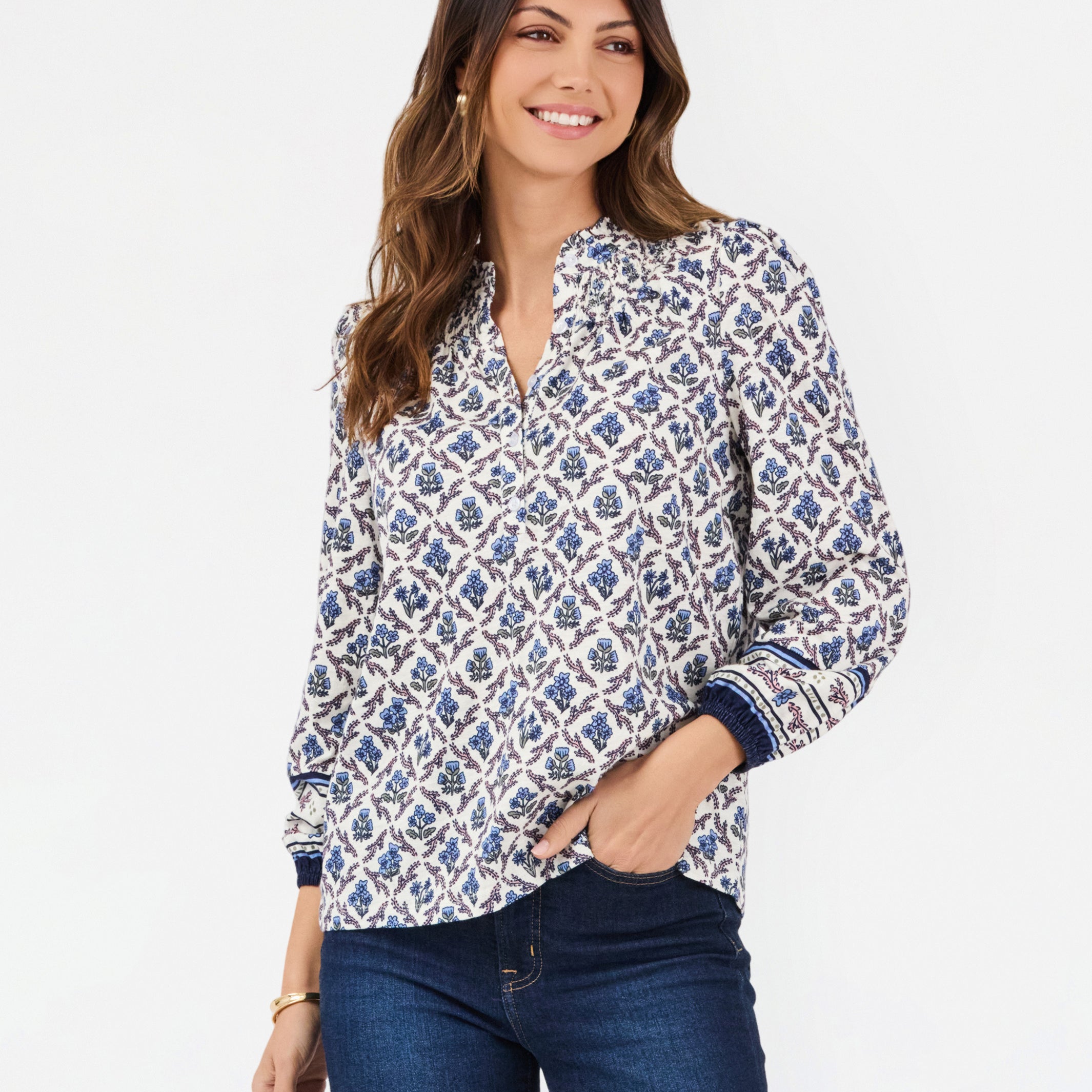 A woman modeling a long-sleeve button-up blouse with a blue and white geometric pattern, paired with dark blue jeans, against a plain white studio background.