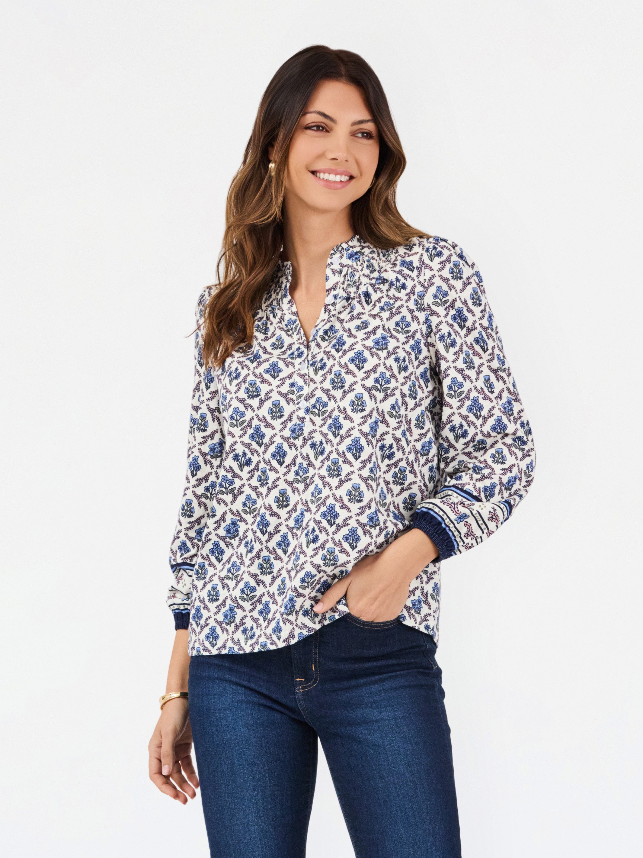 A woman modeling a long-sleeve button-up blouse with a blue and white geometric pattern, paired with dark blue jeans, against a plain white studio background.