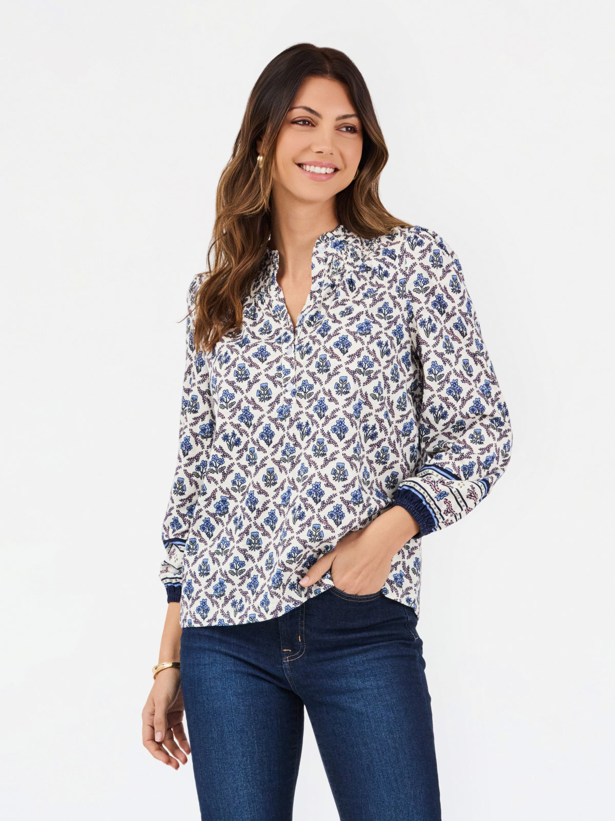 A woman modeling a long-sleeve button-up blouse with a blue and white geometric pattern, paired with dark blue jeans, against a plain white studio background.