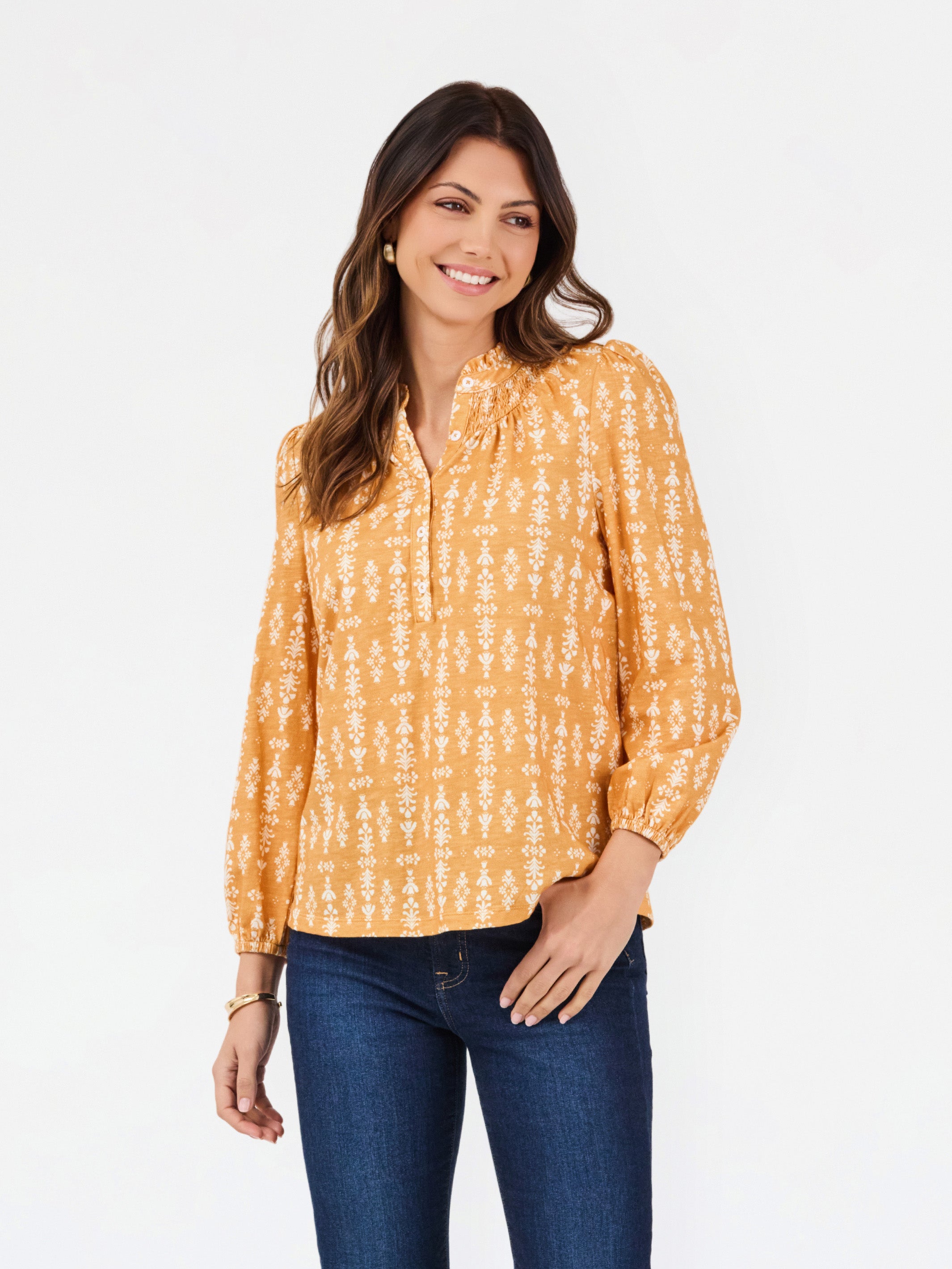 A woman modeling a long-sleeve yellow blouse with a white vertical pattern, paired with dark blue jeans, against a plain white background.