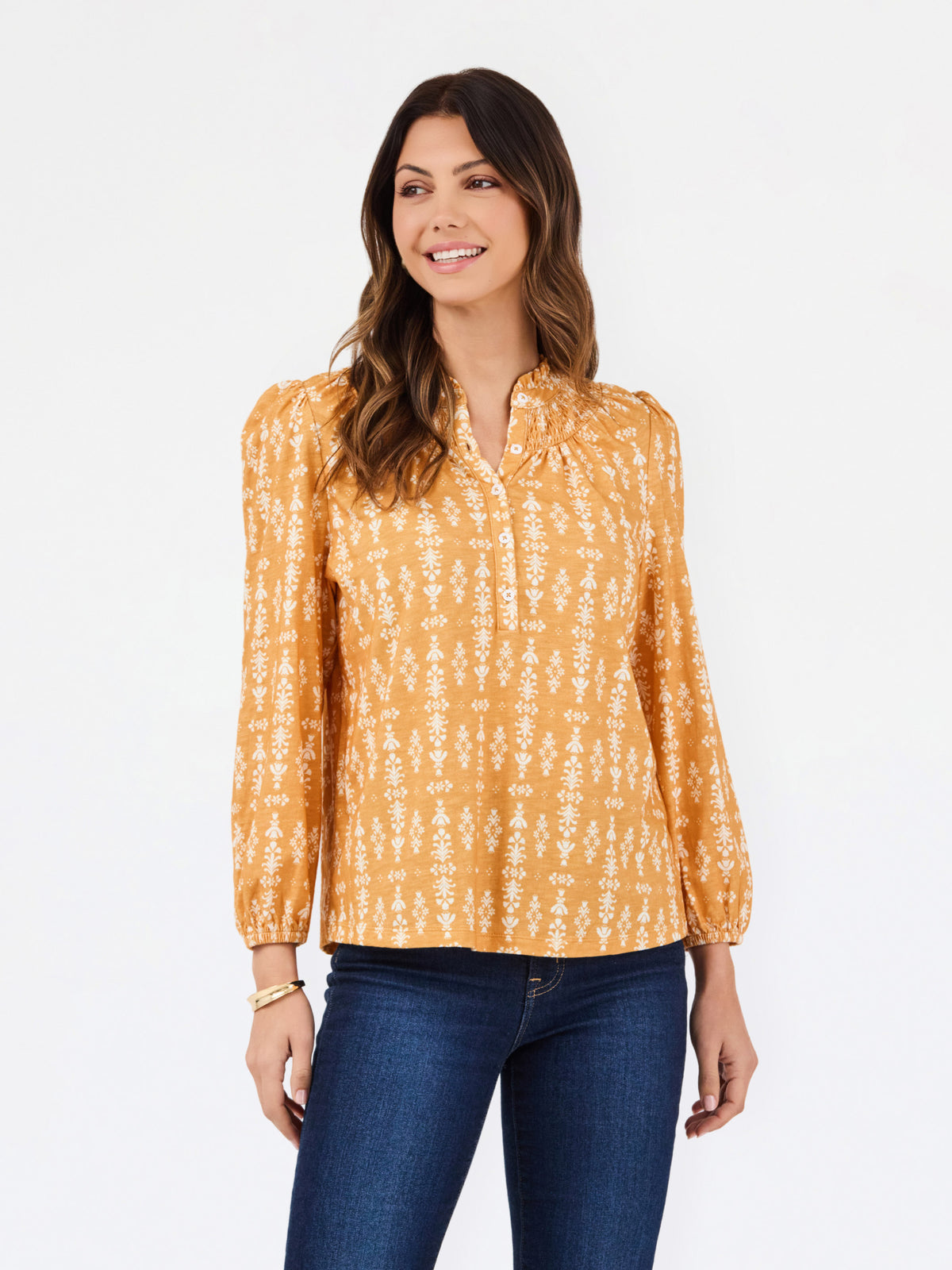 A woman modeling a long-sleeve blouse with a mustard yellow and white vertical pattern, paired with dark blue jeans, against a plain white studio background.