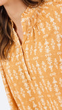 Close-up of a woman wearing a mustard yellow blouse with a white floral print and smocked neckline.