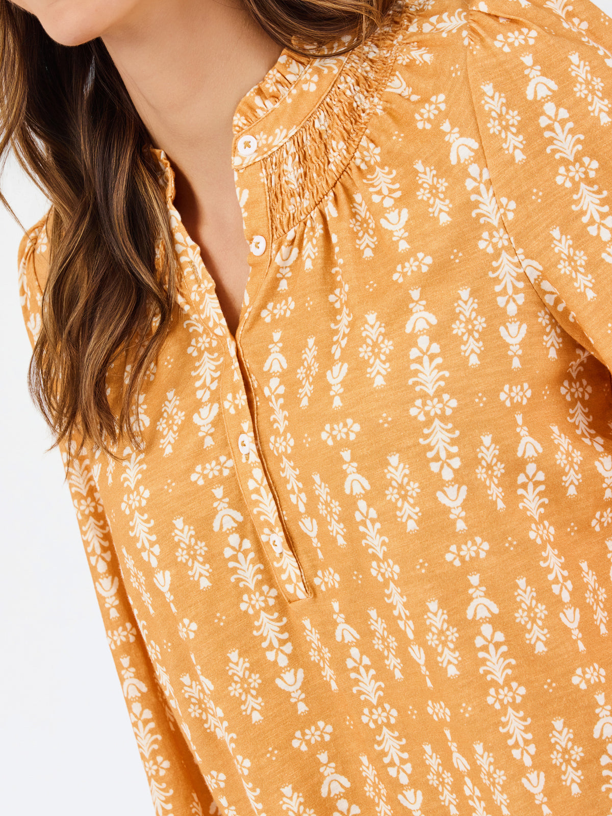 Close-up of a woman wearing a mustard yellow blouse with a white floral print and smocked neckline.