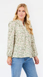 A woman modeling a long-sleeve blouse with a green and beige floral pattern, paired with blue jeans, against a plain white studio background.