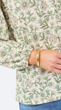 A woman modeling a long-sleeve blouse with a green and beige floral pattern, paired with blue jeans, against a plain white studio background.