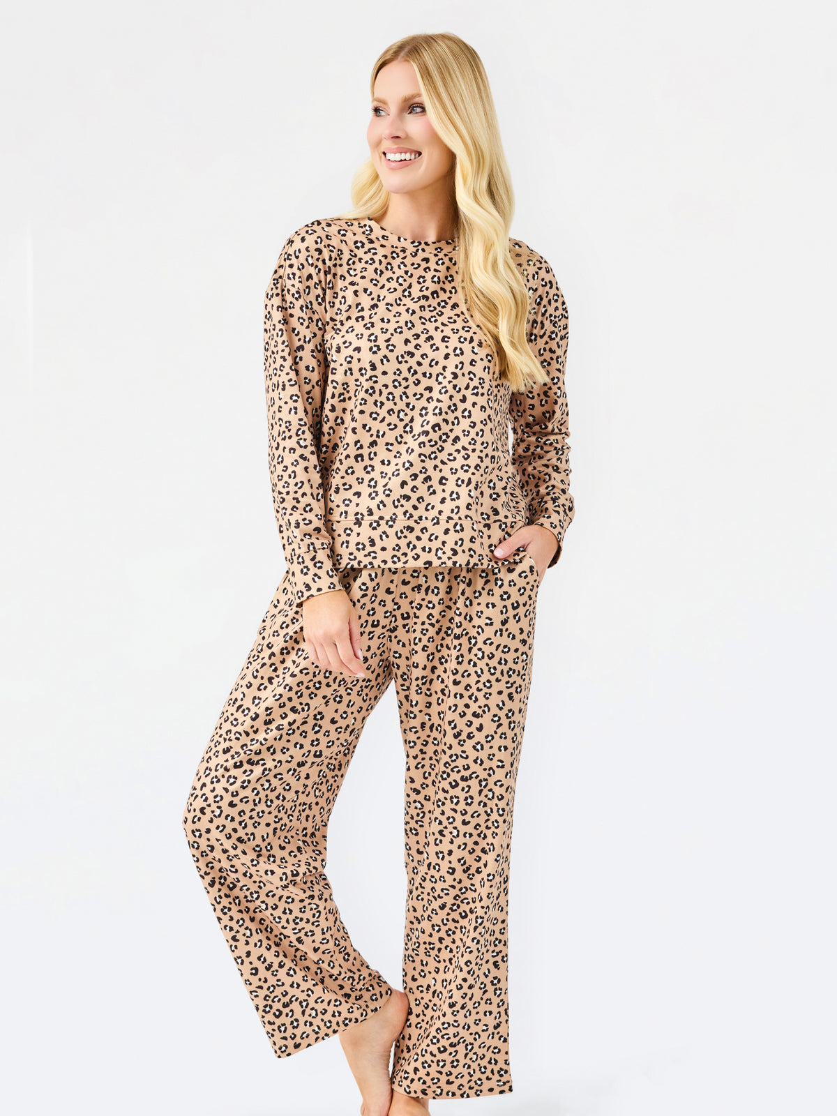 A woman modeling a matching two-piece leopard print pajama set with a long-sleeve top and wide-leg pants, standing against a plain white studio background.
