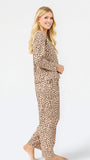 A woman modeling a matching two-piece leopard print pajama set with a long-sleeve top and wide-leg pants, standing against a plain white studio background.