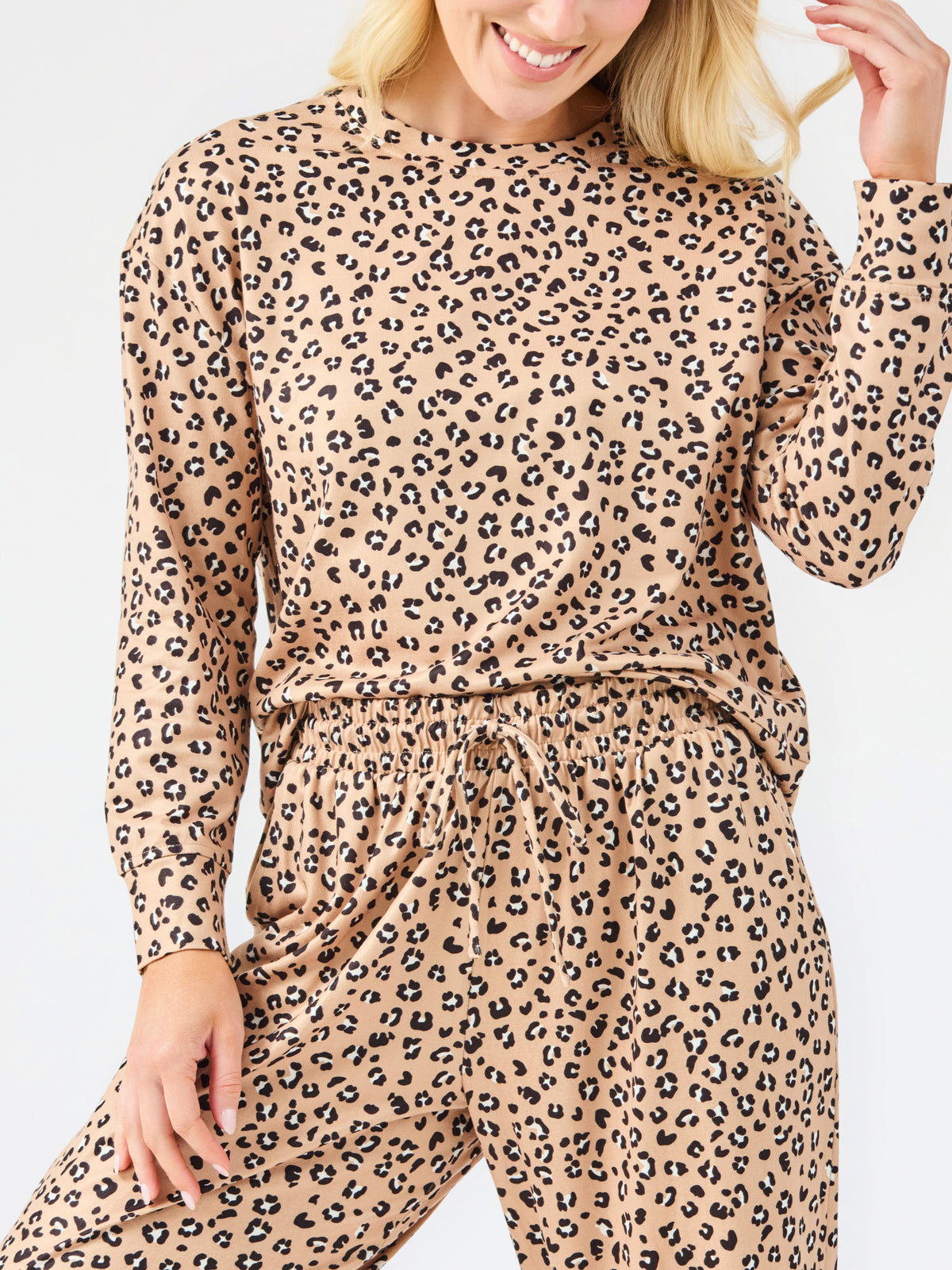 A woman modeling a matching two-piece leopard print pajama set with a long-sleeve top and wide-leg pants, standing against a plain white studio background.