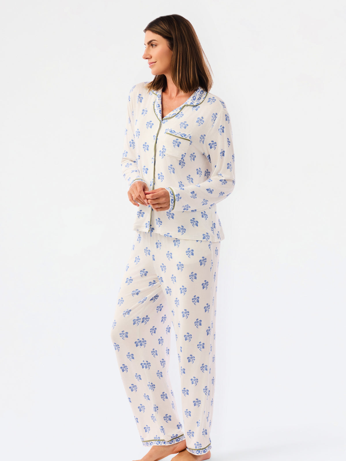 A woman modeling a two-piece pajama set with a white base and blue floral pattern, standing against a plain white studio background.