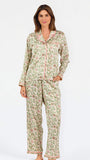 A woman modeling a two-piece pajama set with a long-sleeve button-front top and matching wide-leg pants, featuring a light beige base with a green and pink floral pattern, set against a plain white studio background.