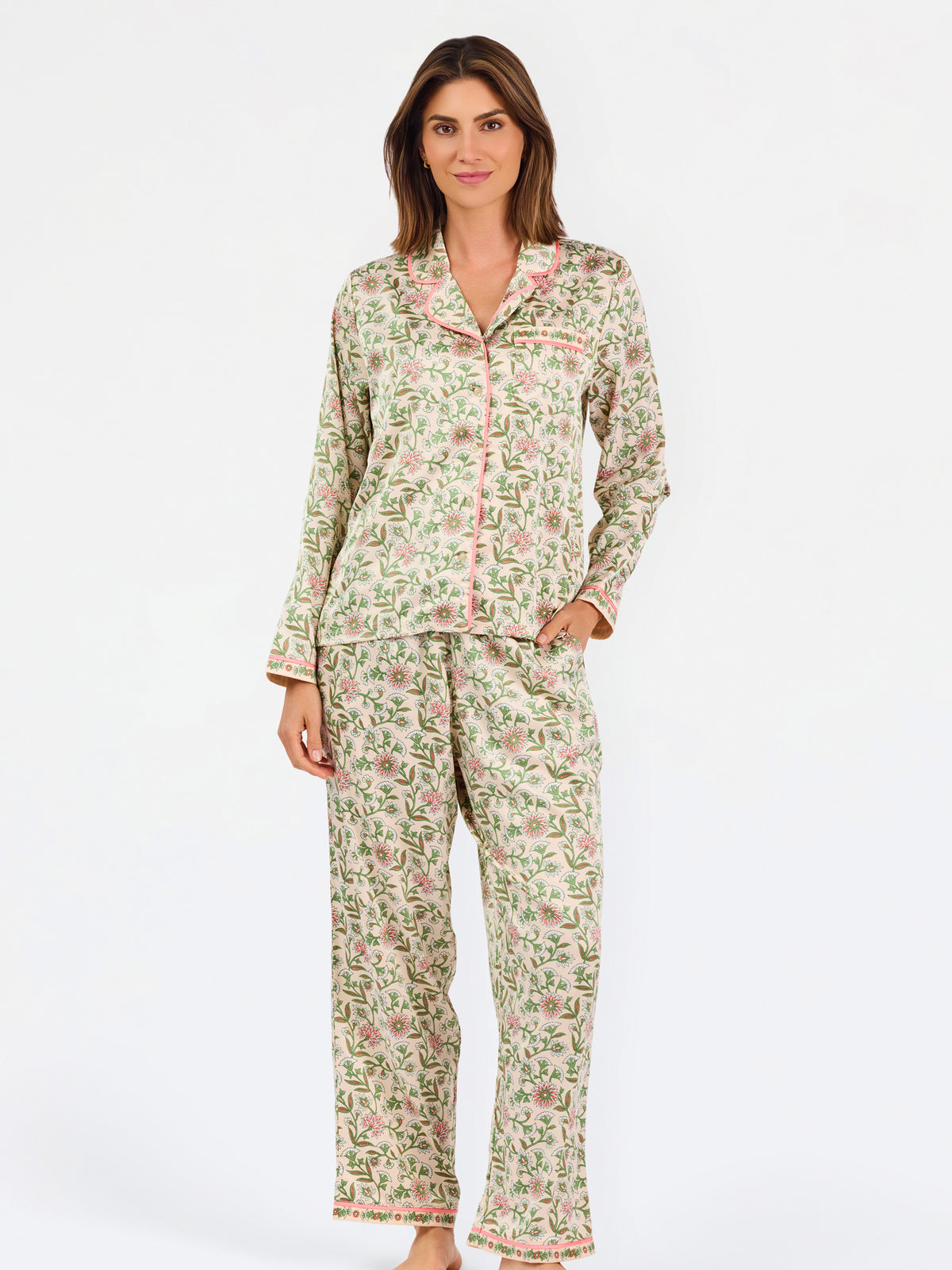 A woman modeling a two-piece pajama set with a long-sleeve button-front top and matching wide-leg pants, featuring a light beige base with a green and pink floral pattern, set against a plain white studio background.