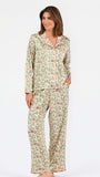 A woman modeling a two-piece pajama set with a long-sleeve button-front top and matching wide-leg pants, featuring a light beige base with a green and pink floral pattern, set against a plain white studio background.