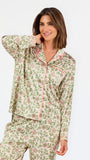 A woman modeling a two-piece pajama set with a long-sleeve button-front top and matching wide-leg pants, featuring a light beige base with a green and pink floral pattern, set against a plain white studio background.
