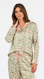 A woman modeling a two-piece pajama set with a long-sleeve button-front top and matching wide-leg pants, featuring a light beige base with a green and pink floral pattern, set against a plain white studio background.