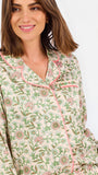 A woman modeling a two-piece pajama set with a long-sleeve button-front top and matching wide-leg pants, featuring a light beige base with a green and pink floral pattern, set against a plain white studio background.