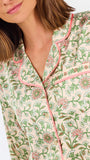 A woman modeling a two-piece pajama set with a long-sleeve button-front top and matching wide-leg pants, featuring a light beige base with a green and pink floral pattern, set against a plain white studio background.