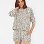 A woman modeling a matching two-piece loungewear set featuring a beige and black leopard print pattern, consisting of a long-sleeve top and shorts, against a plain white studio background.