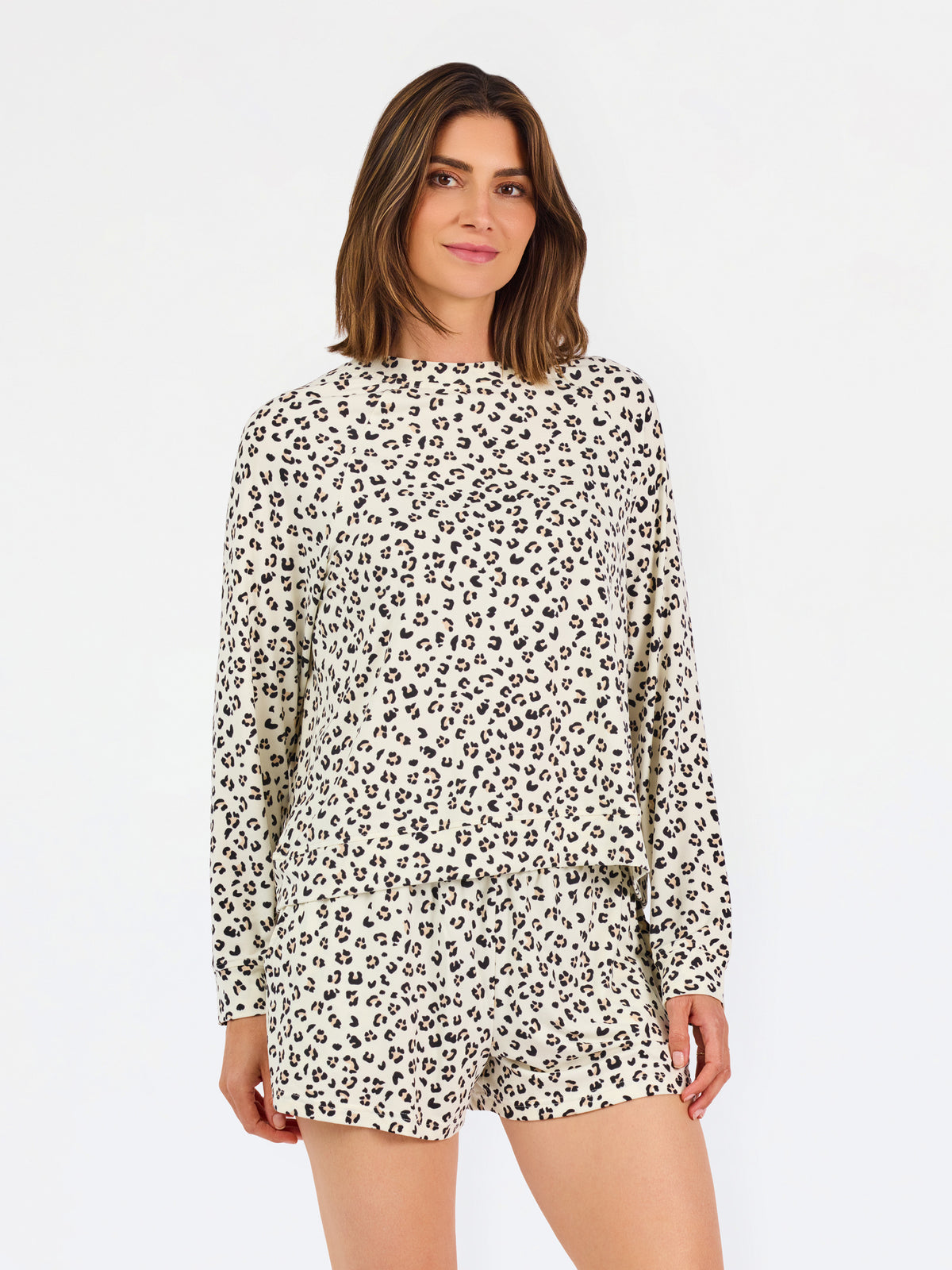 A woman modeling a matching two-piece loungewear set featuring a beige and black leopard print, consisting of a long-sleeve top and shorts, against a plain white studio background.