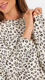 A woman modeling a matching two-piece loungewear set featuring a beige and black leopard print pattern, consisting of a long-sleeve top and shorts, against a plain white studio background.