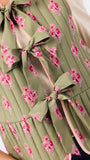 Close-up of a sleeveless quilted vest in olive green with a pink and white floral print, featuring large bow details at the front.