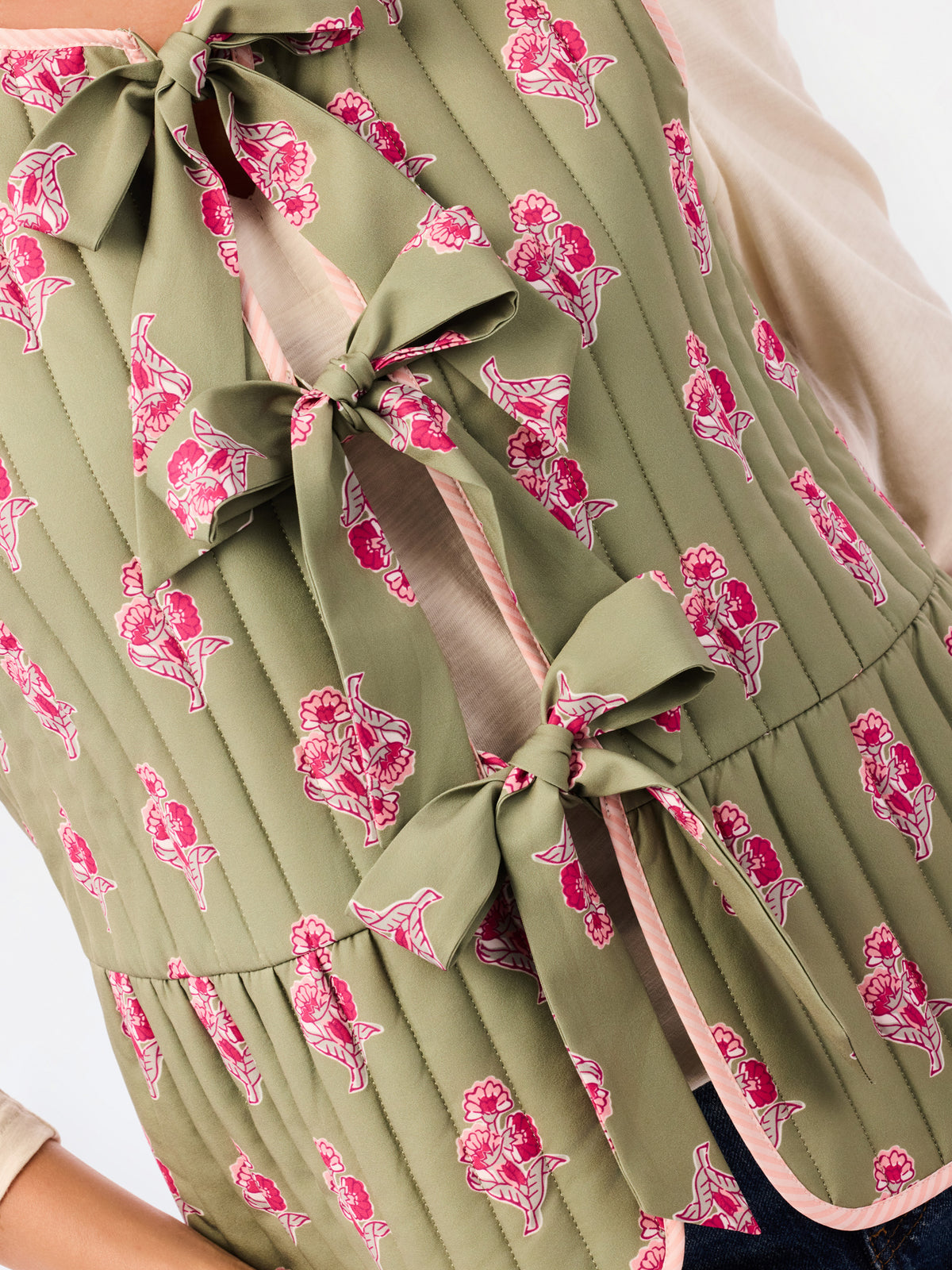 Close-up of a sleeveless quilted vest in olive green with a pink and white floral print, featuring large bow details at the front.
