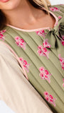 Close-up of a model wearing a quilted olive green vest with a pink floral pattern and a matching bow at the neckline, layered over a light beige blouse.